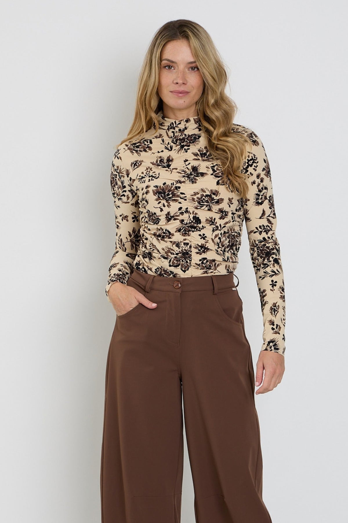 Mi Piace Travel Top met sierlijke bloemenprint, lichtgewicht zandkleurig, met wriemkellijn en ornamentale details.