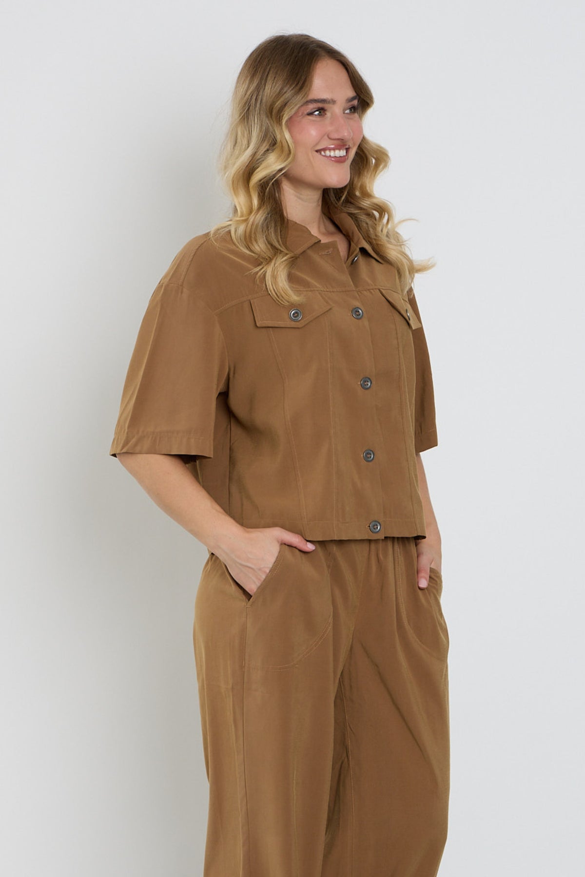 Camelkleurige Enjoy jas met knoopsluiting en stijlvolle details, zichtbaar met close-up van knoop en stofstructuur.
