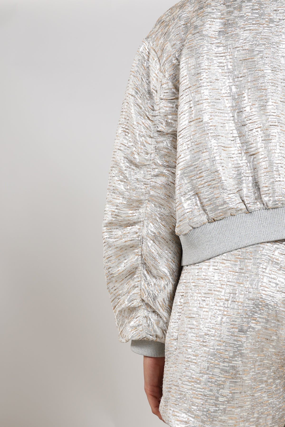 Nukus Babette Silver Camel jas met glanzende afwerking, korte pasvorm, en capuchon, gedragen door een model.