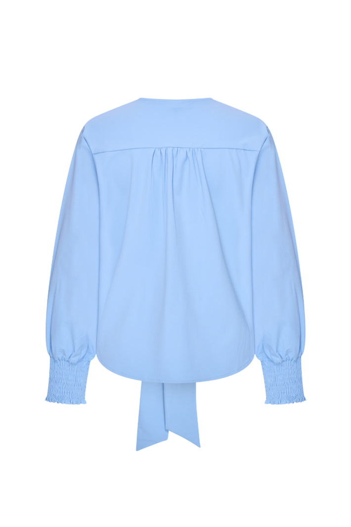 Mi Piace Travel Top Knotted Della Blue, blauw top met knoopdetail, gedragen door een model met lichte achtergrond.