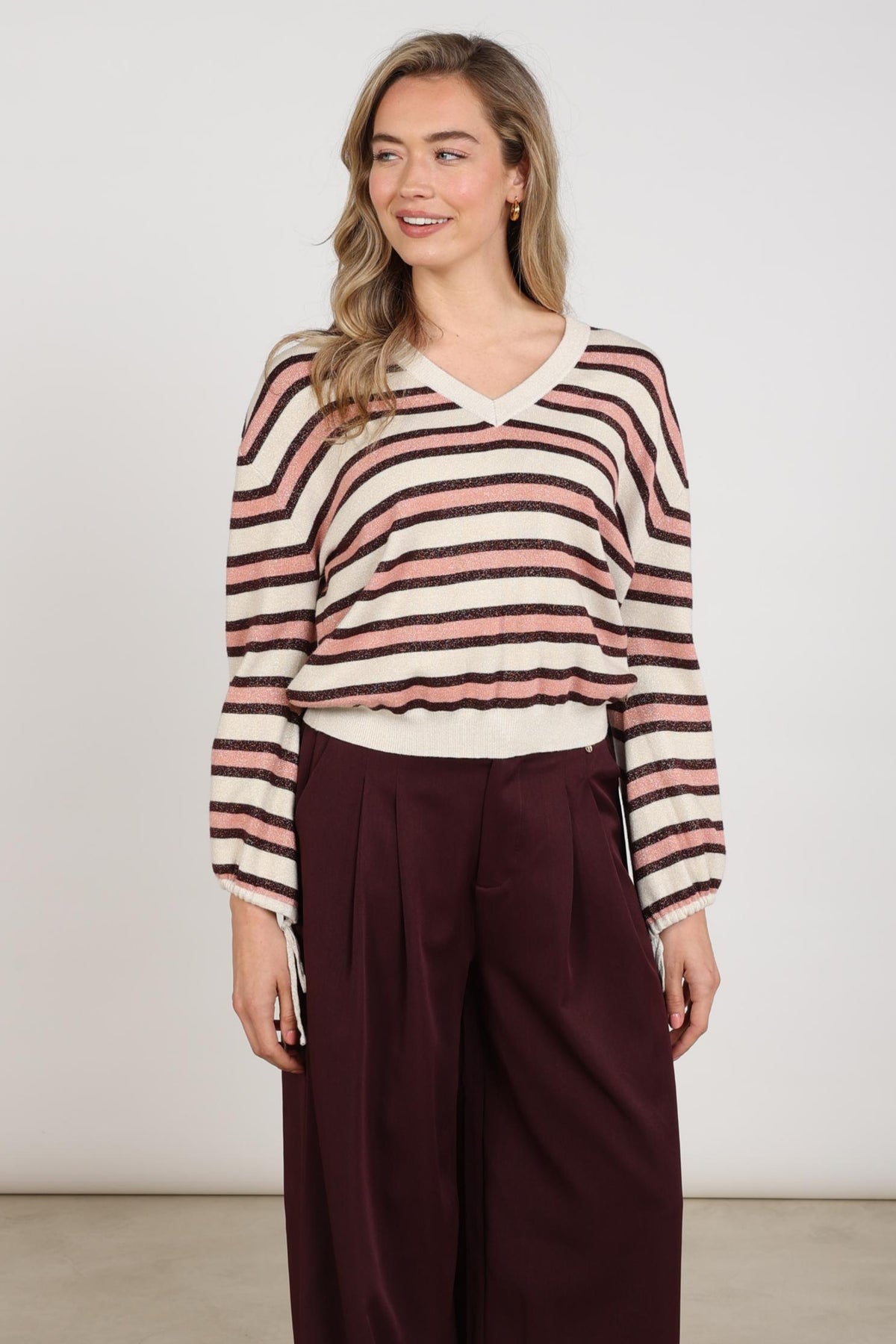 Nukus Kim Stripe Sand Rose trui met roze en beige strepen, zachte gebreide stof, gedragen door een model in een lichte setting