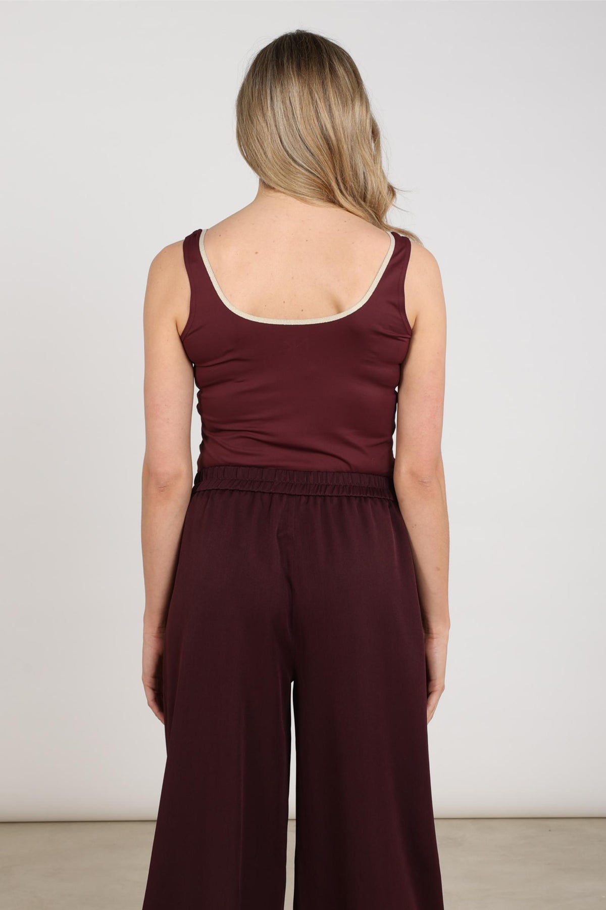 Nukus Juba Cherry Gold singlet met goudkleurig ontwerp, close-up van de stof en het patroon op een effen achtergrond