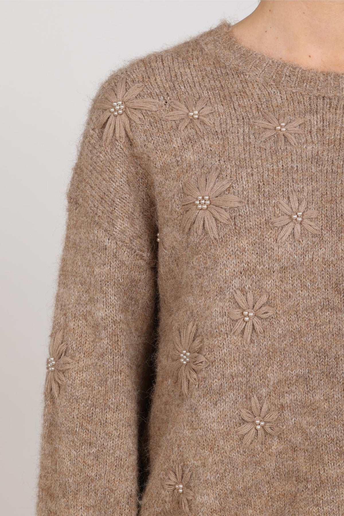 Taupe gekleurde trui Konstanza Flower van Nukus, met bloemendessin, gedragen door een persoon op een neutrale achtergrond.