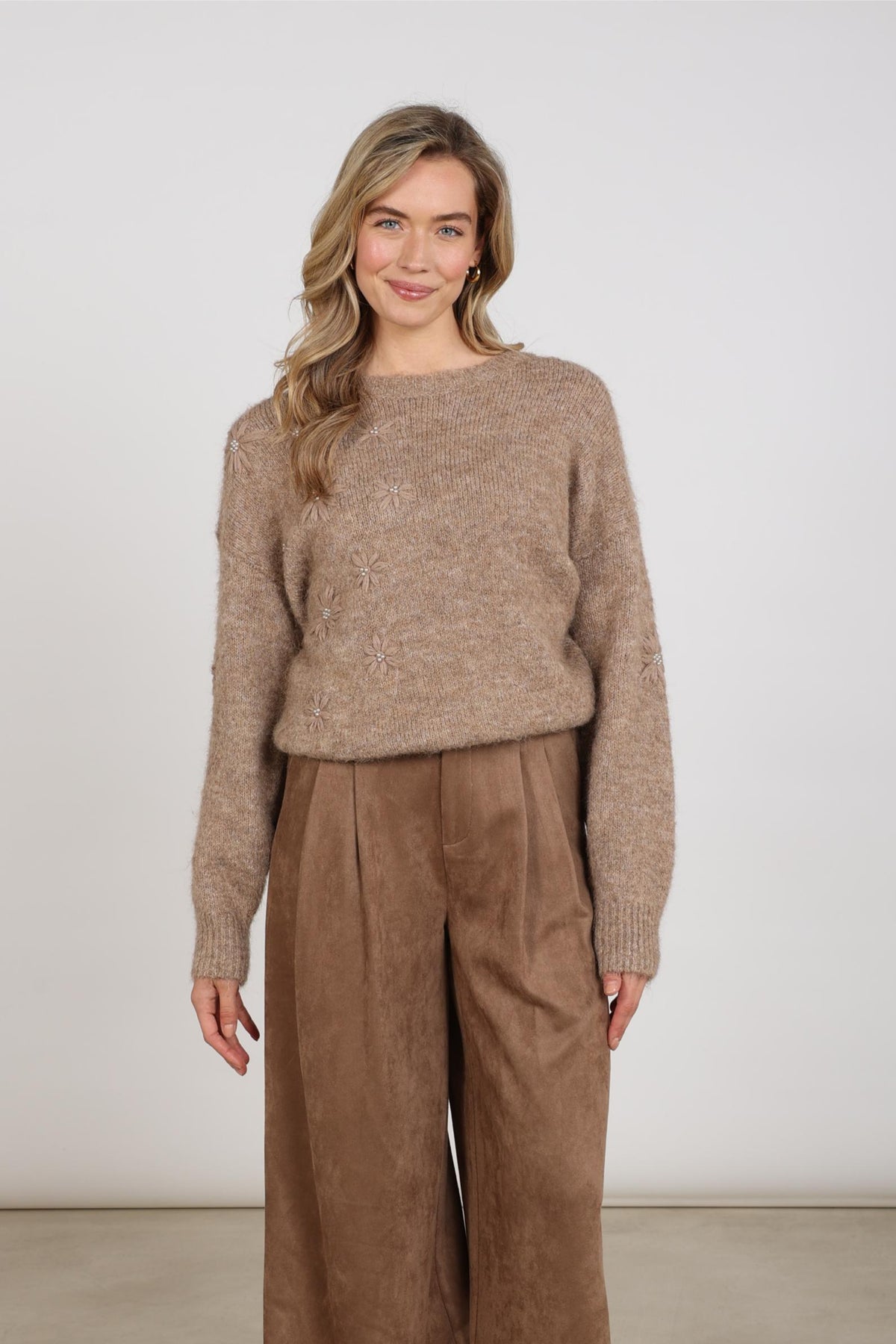 Taupe trui Konstanza Flower van Nukus met bloemendessin, zachte stof en comfortabele pasvorm, zichtbaar in de afbeelding.