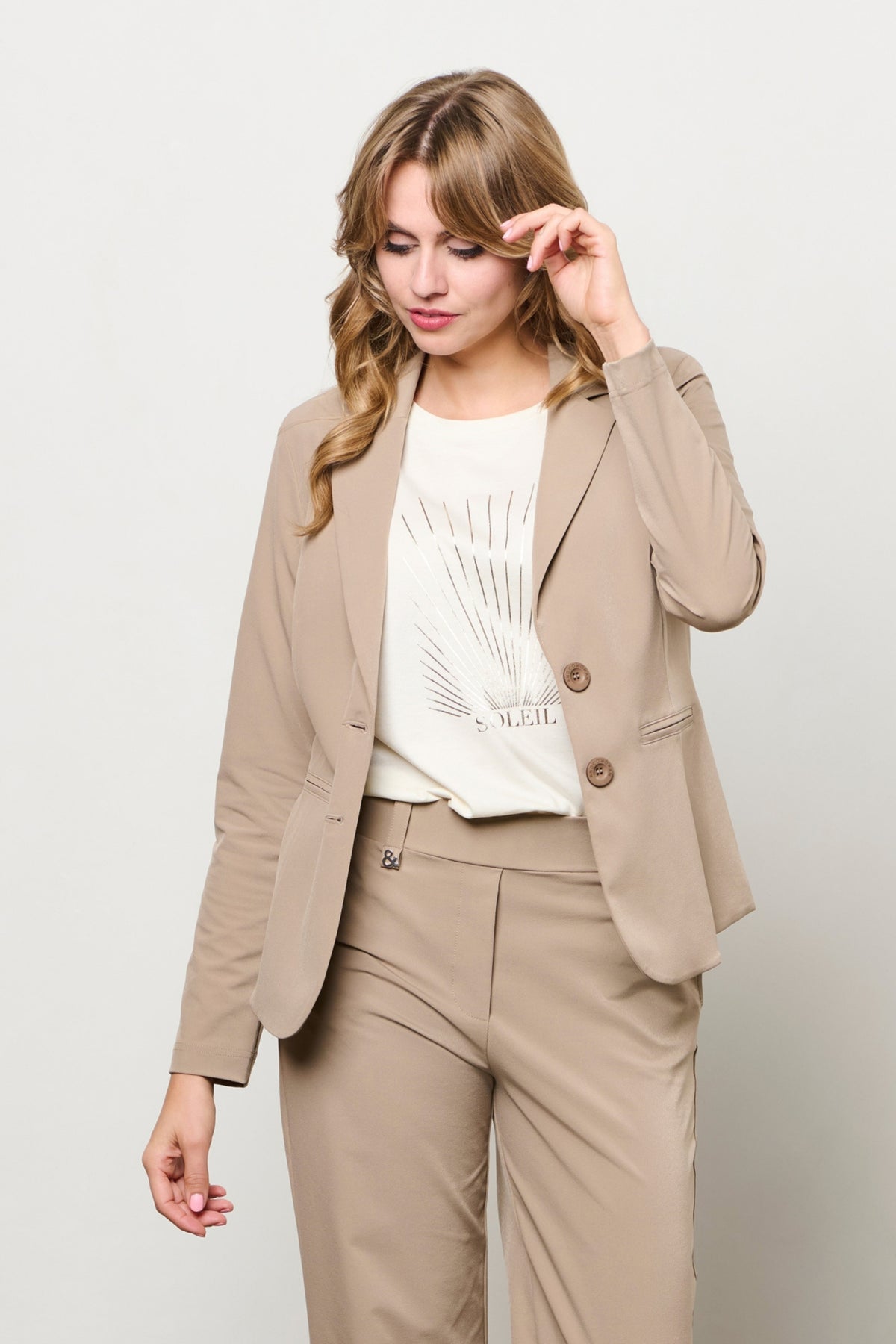 Taupe reisblazer van &Co woman, model Phileine, met stijlvolle snit en knoopsluiting, gedragen door een vrouw.