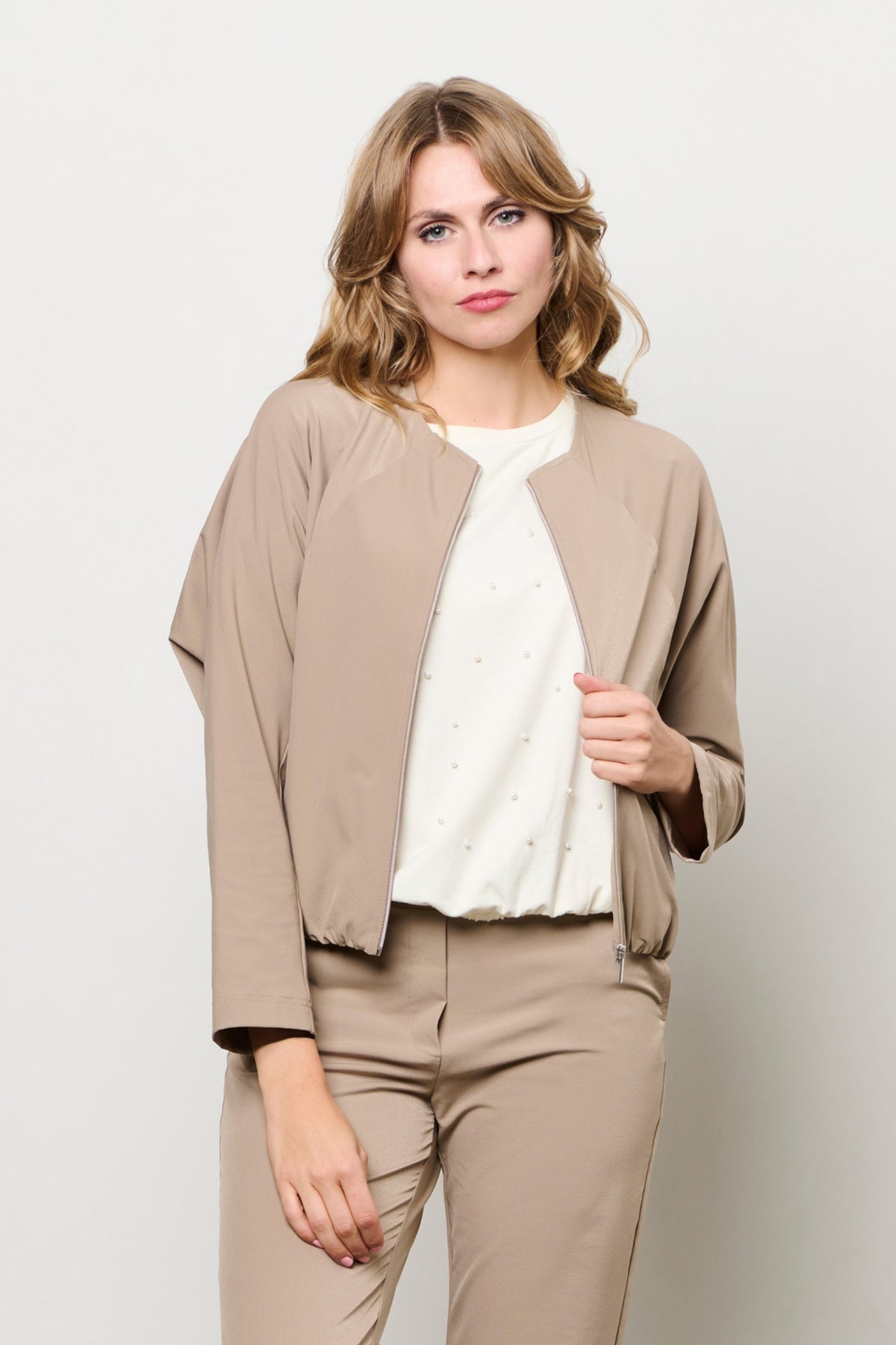 Reisjasje Pihla in taupe van &Co woman, getailleerd met ritssluiting en capuchon, gedragen door een model.