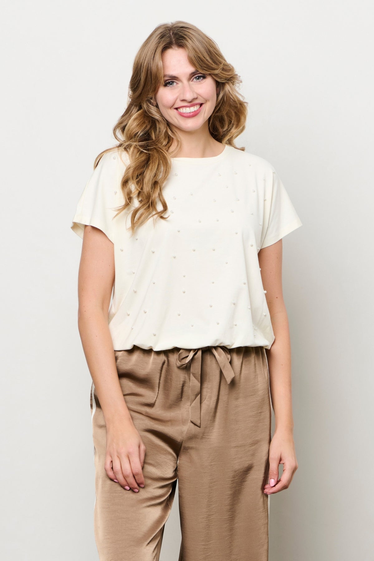 Licht beige top Terese van &Co woman, modieus en comfortabel, met subtiele details, op een witte achtergrond.