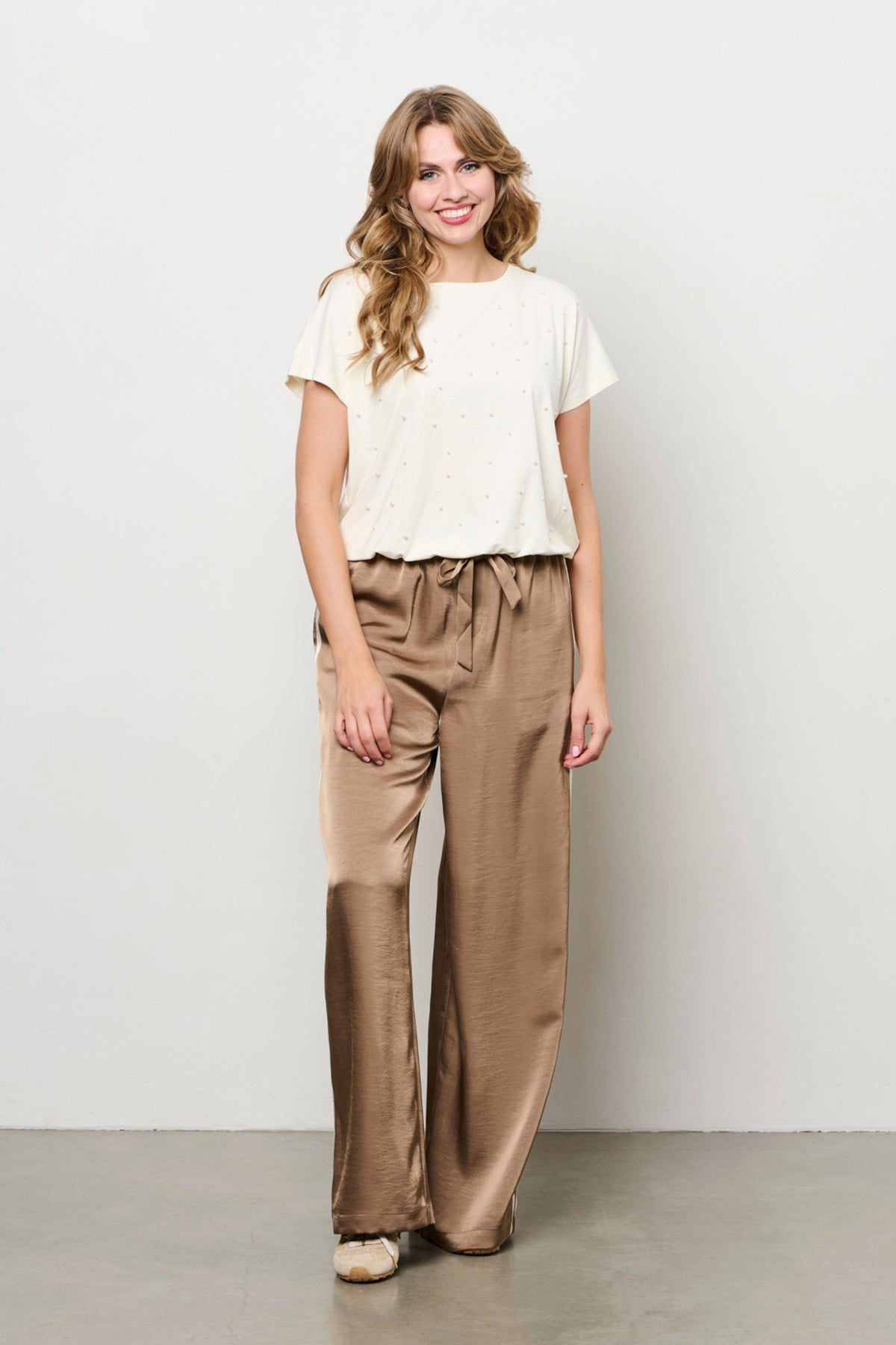 Beige top Terese van &Co woman, soepel vallend met korte mouwen en ronde hals, gedragen door een model.