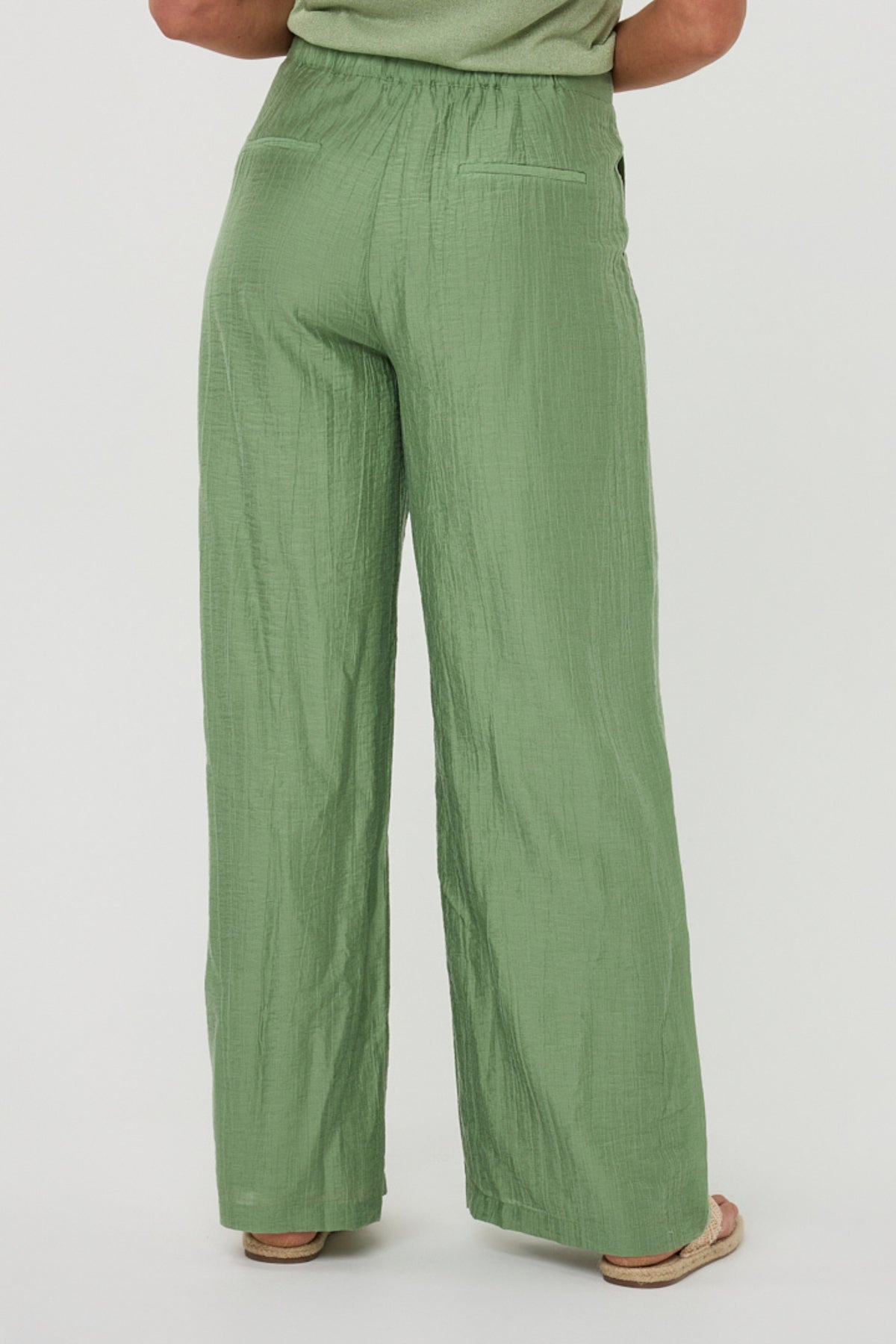 Lichte jungle groene wide fit crinkle broek van EsQualo, model Larissa, getoond in een natuurlijke pose.