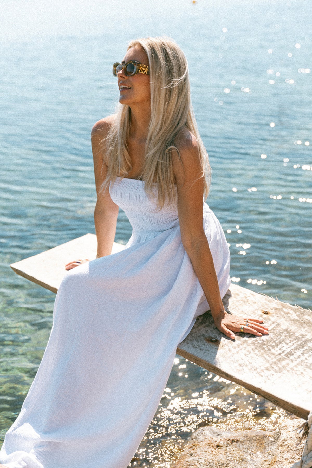 Strandjurk van Bolina Island, strapless en wit, met losse fit en elegante uitstraling, gedragen door een model op een zonnige achtergrond.