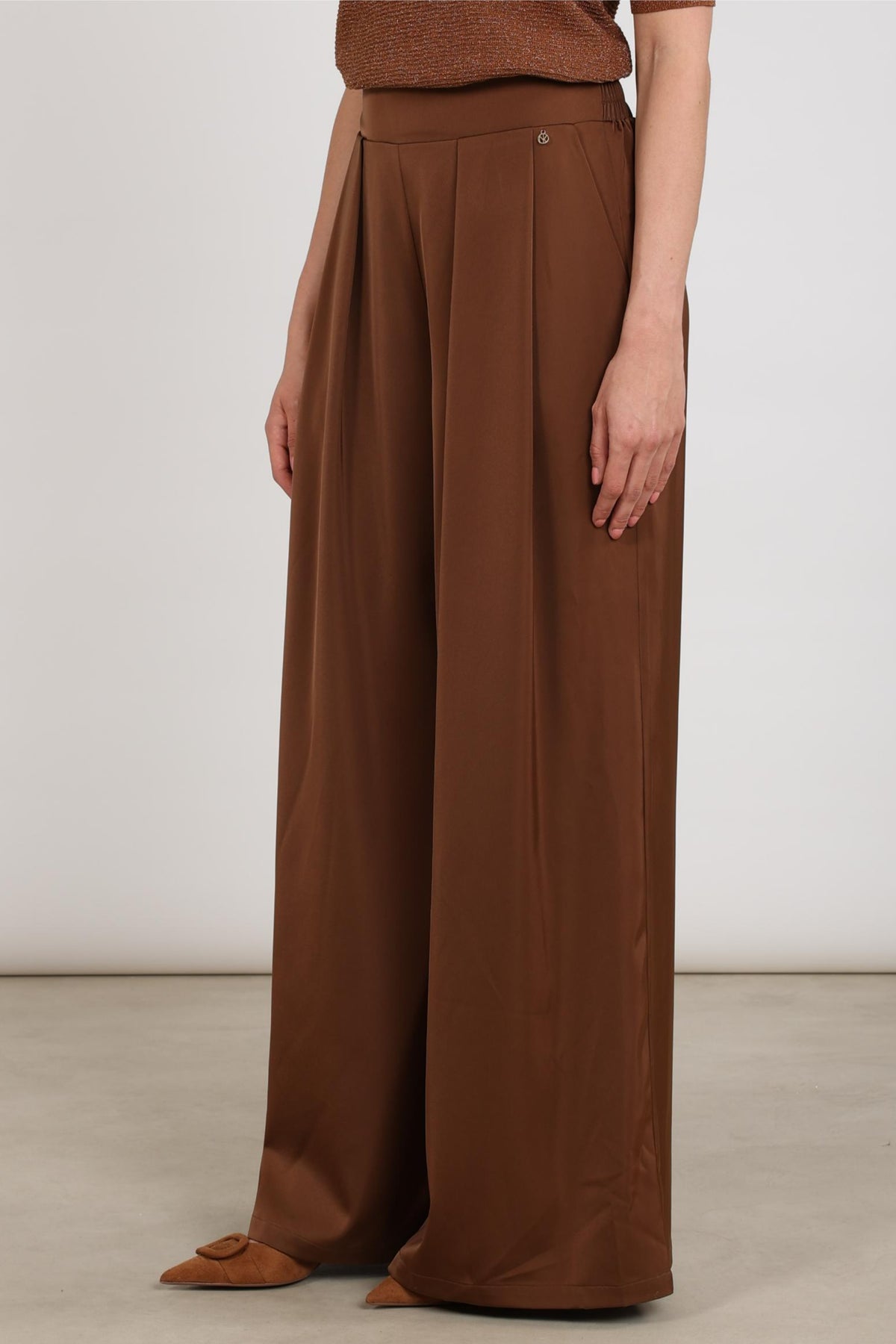 Nukus broek June Shiny Espresso, glanzende donkerbruine damesbroek met tailleband en rechte snit, gedragen door een model.