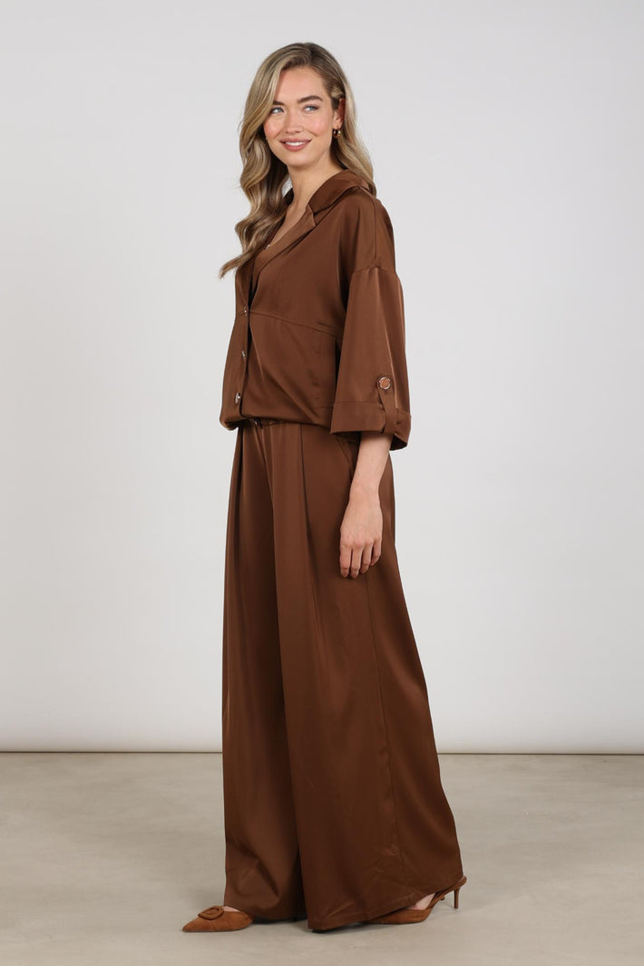 Glanzende espresso Nukus broek June Shiny met smalle pasvorm en elastische taille, gedragen door een model op de foto