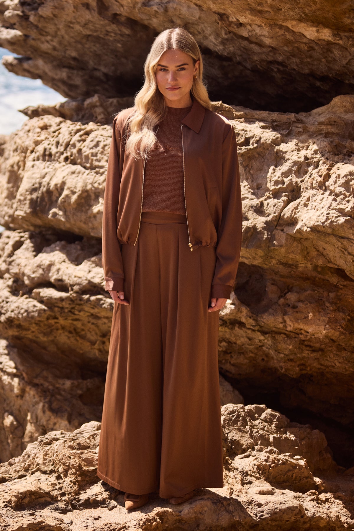 Nukus June Shiny Espresso broek, gladde stof en elastische taille, gedragen door een model op een lichte achtergrond.