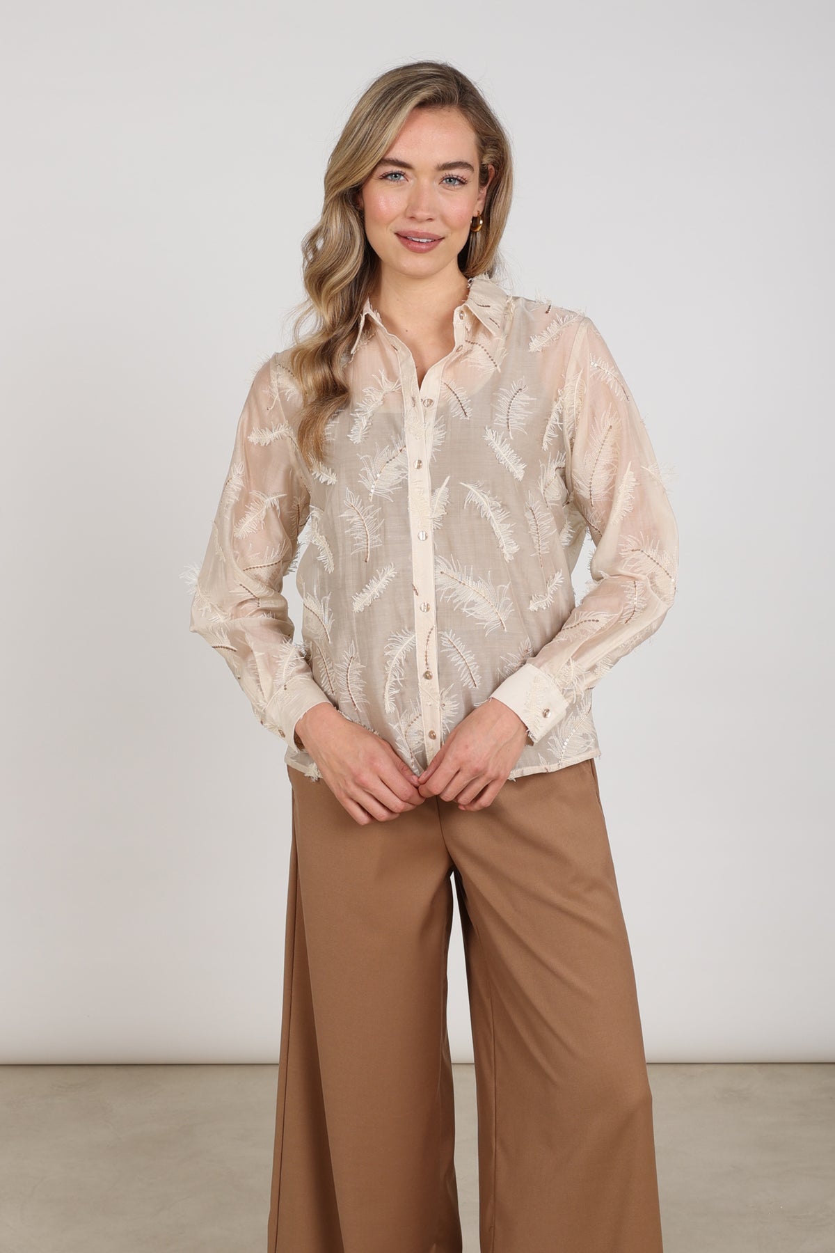 Nukus blouse Aysha met veren in zandkleur, elegante damesblouse met details, op een witte achtergrond.
