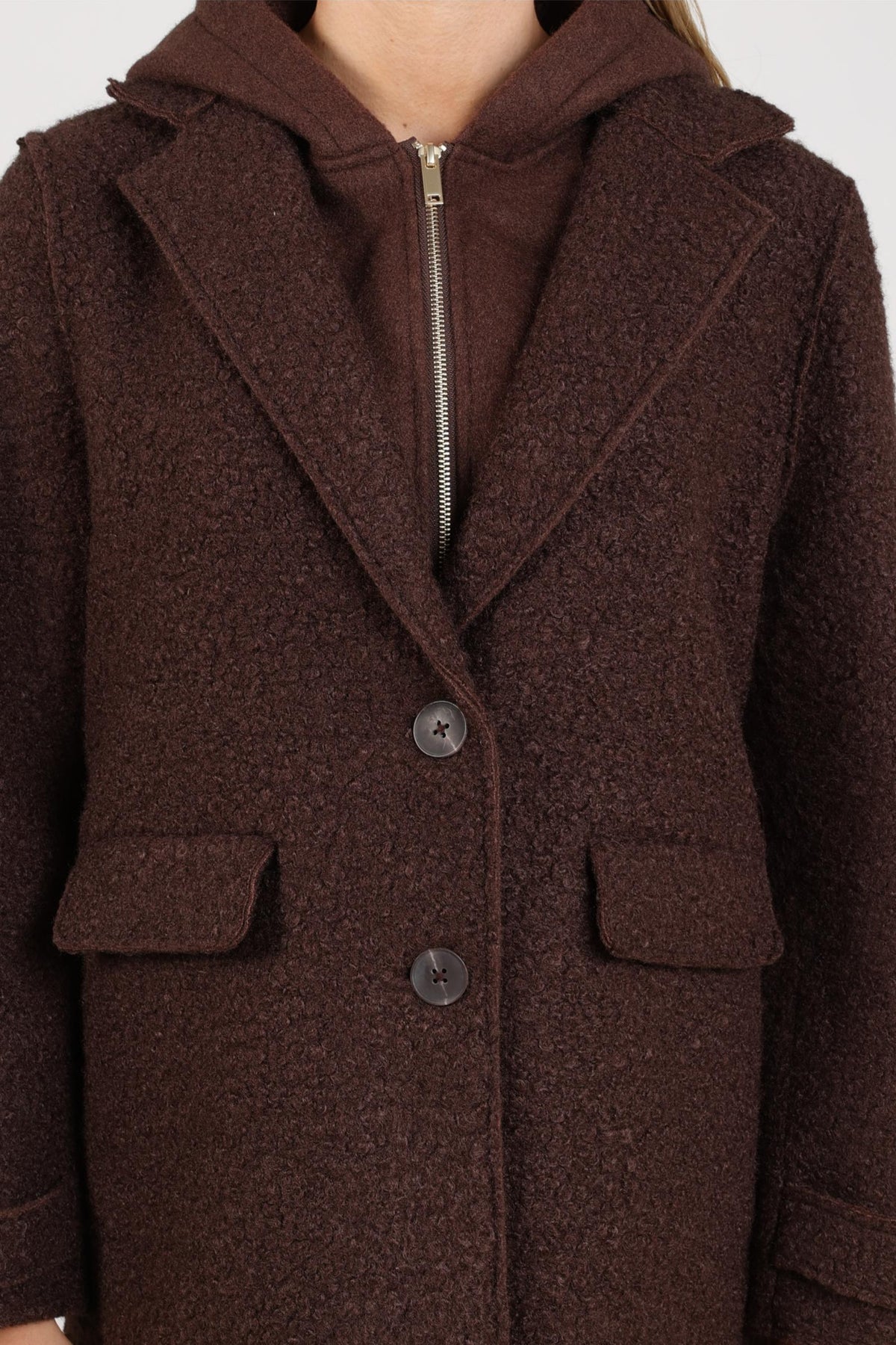 Donkerbruine boucle jas Mirthe van Nukus met stijlvolle kraag en knopen, gedragen door een model op een lichte achtergrond.