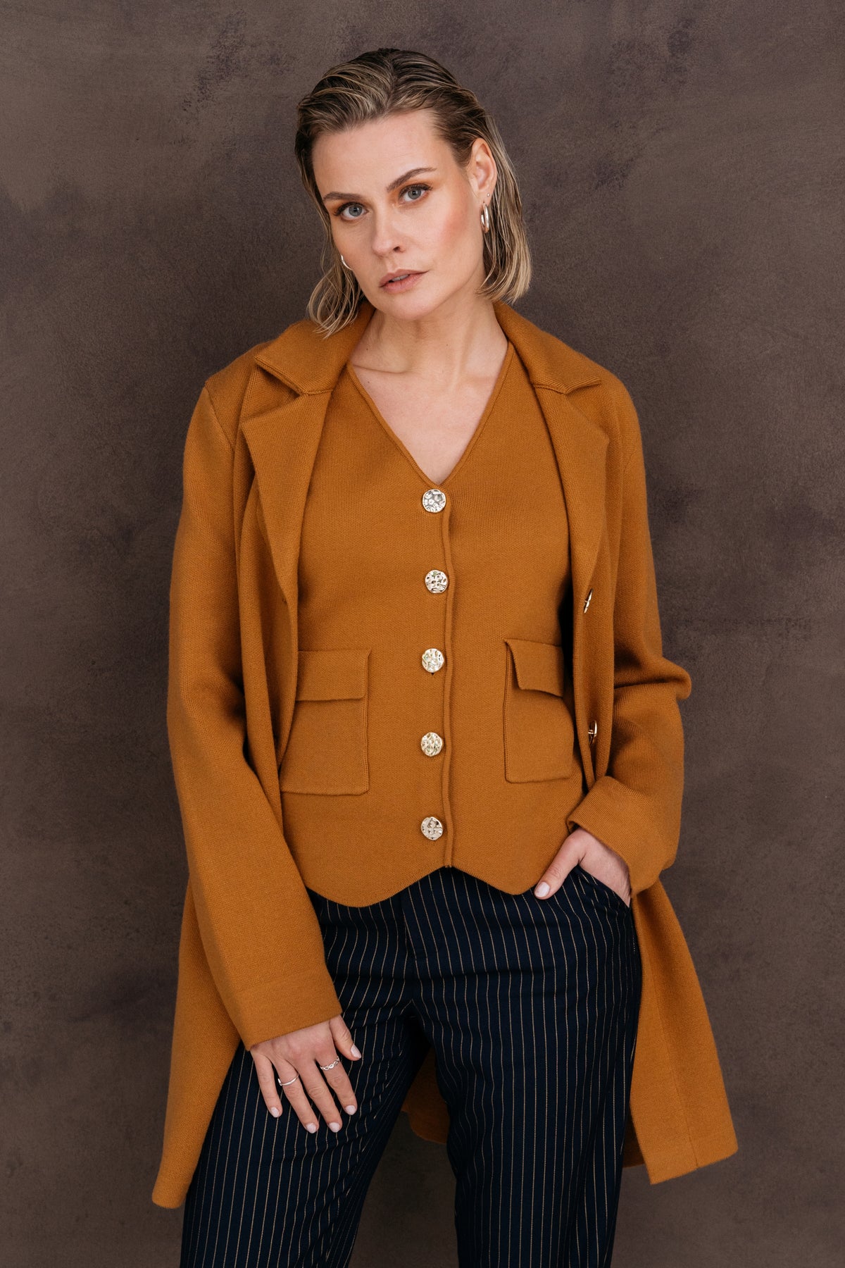 Lange beige vest met Pessie Apple Cinnamon patroon en knopen, gedragen door model op wit achtergrond.