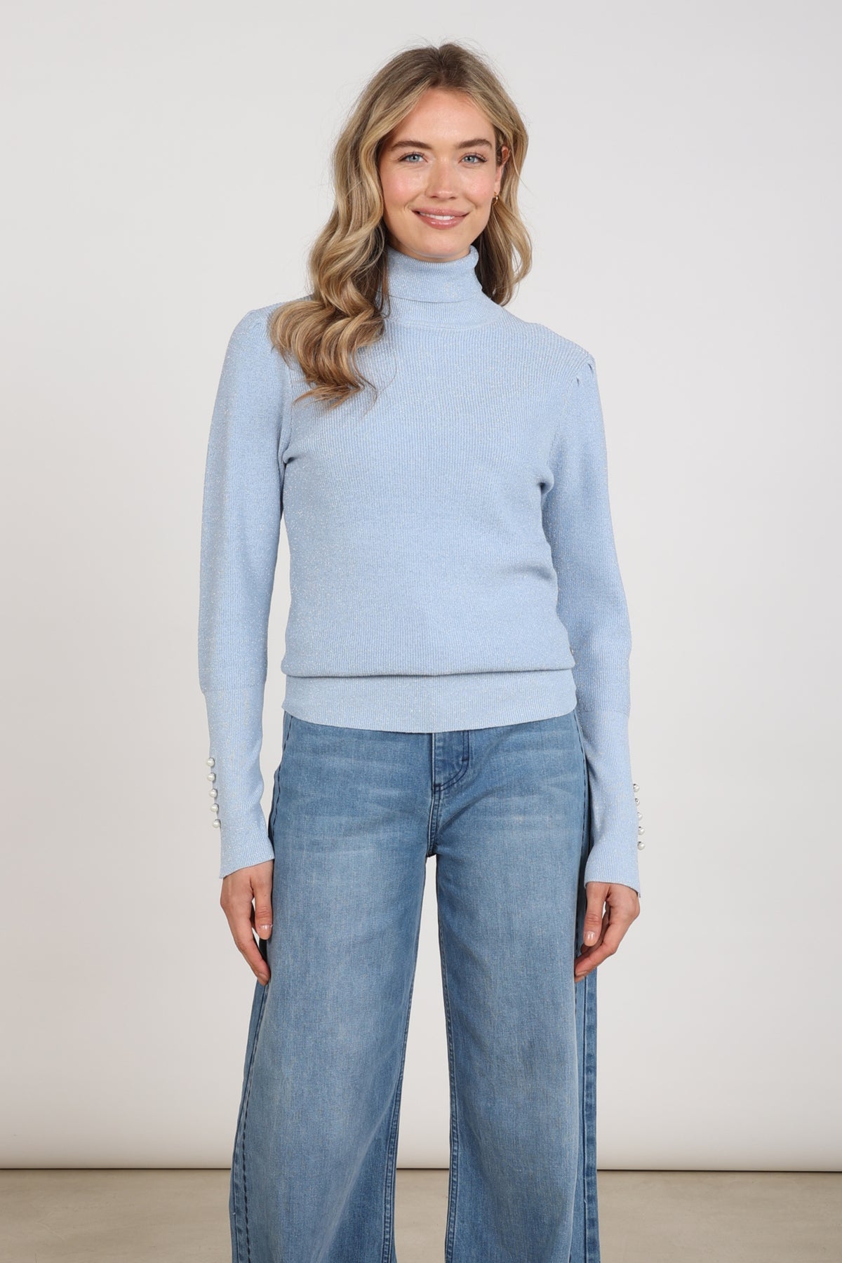 Donkere blauwe trui Sylvia Lurex van Nukus met glanzende lurex-details, gedragen door een model op een witte achtergrond.