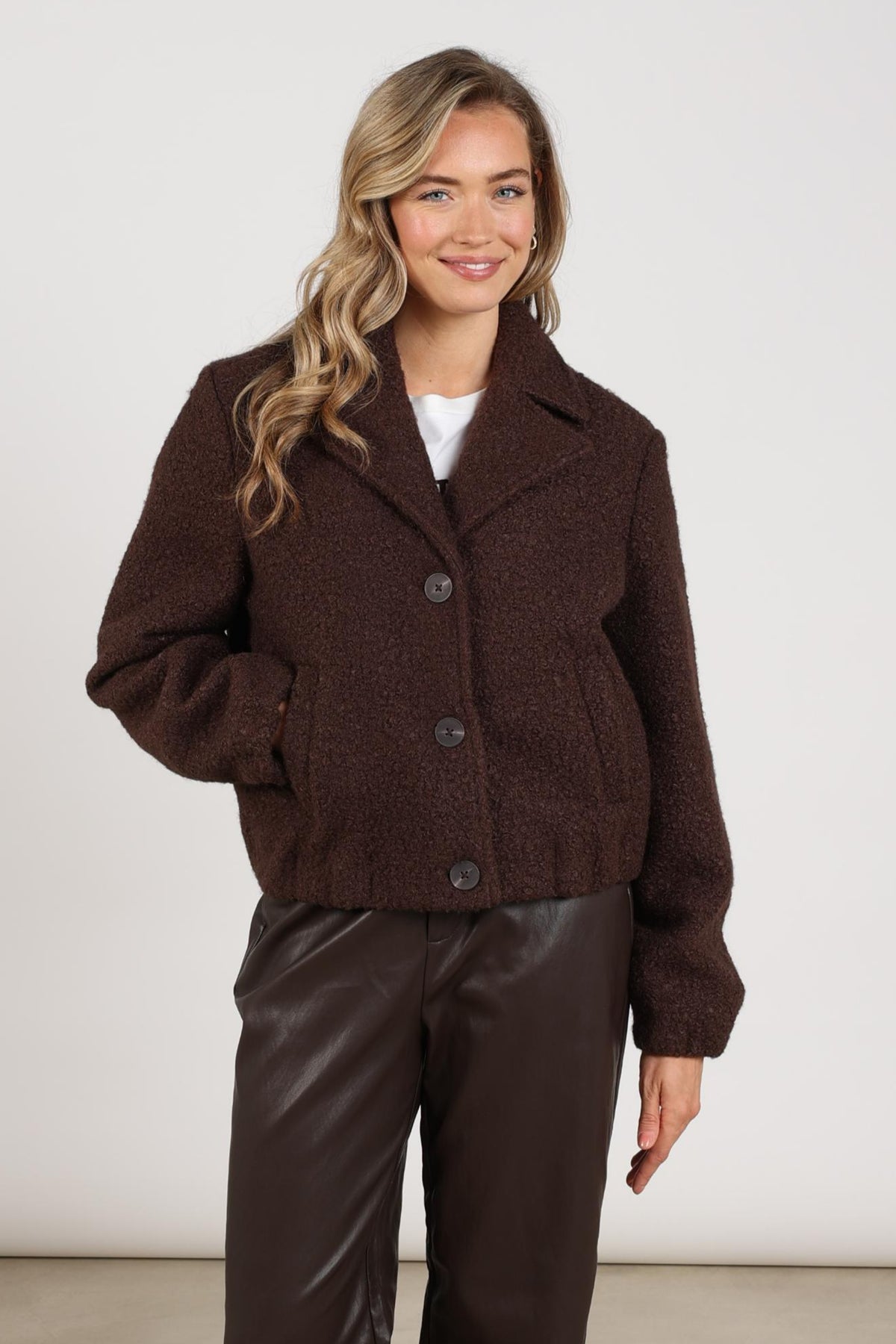 Donkere chocolade boucle jas Madelin van Nukus, getoond op een model met de jas open en dicht, stijlvolle winterjas.