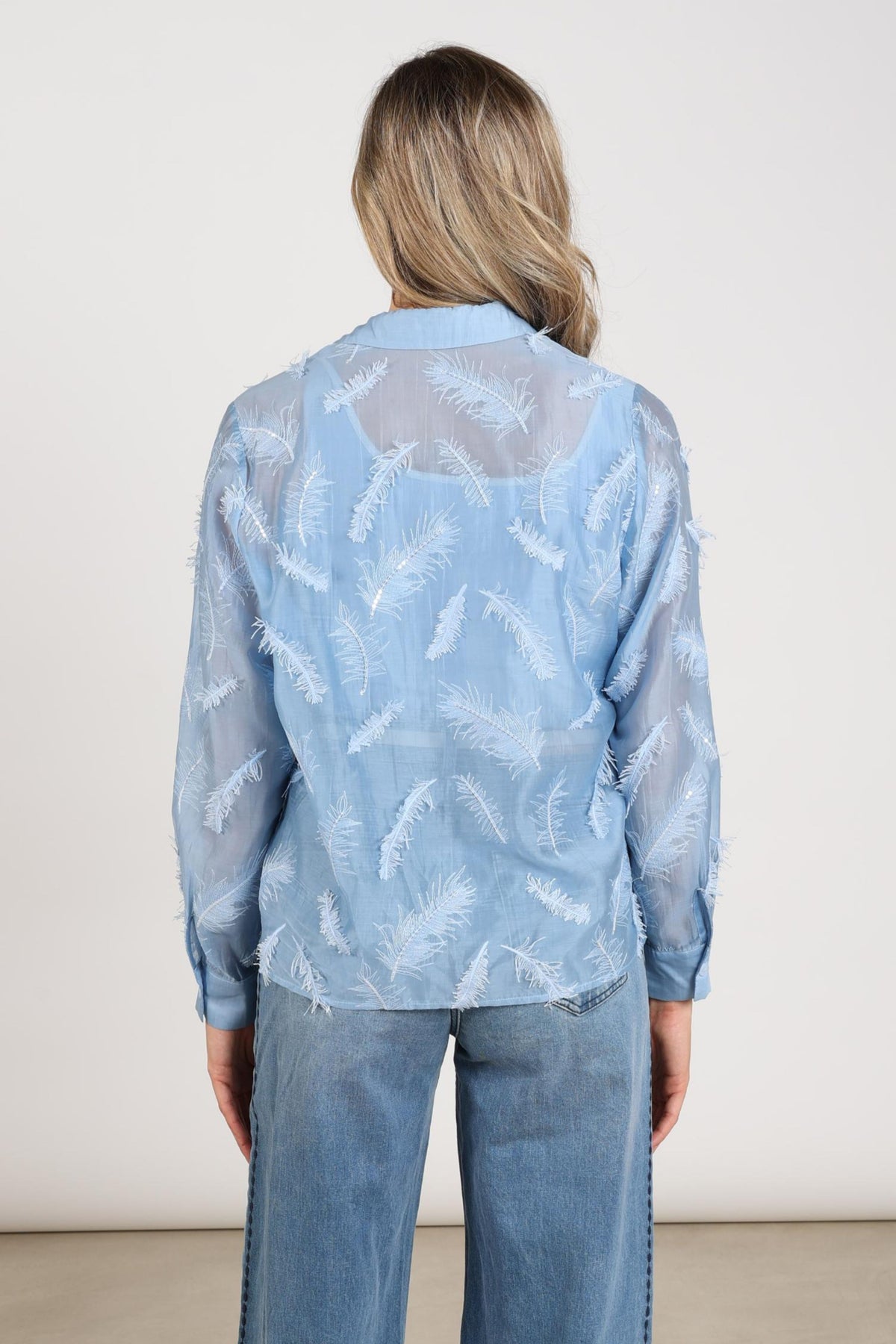 Lichte blauwe blouse Aysha met verenprint en lange mouwen van Nukus, gedragen door een model.