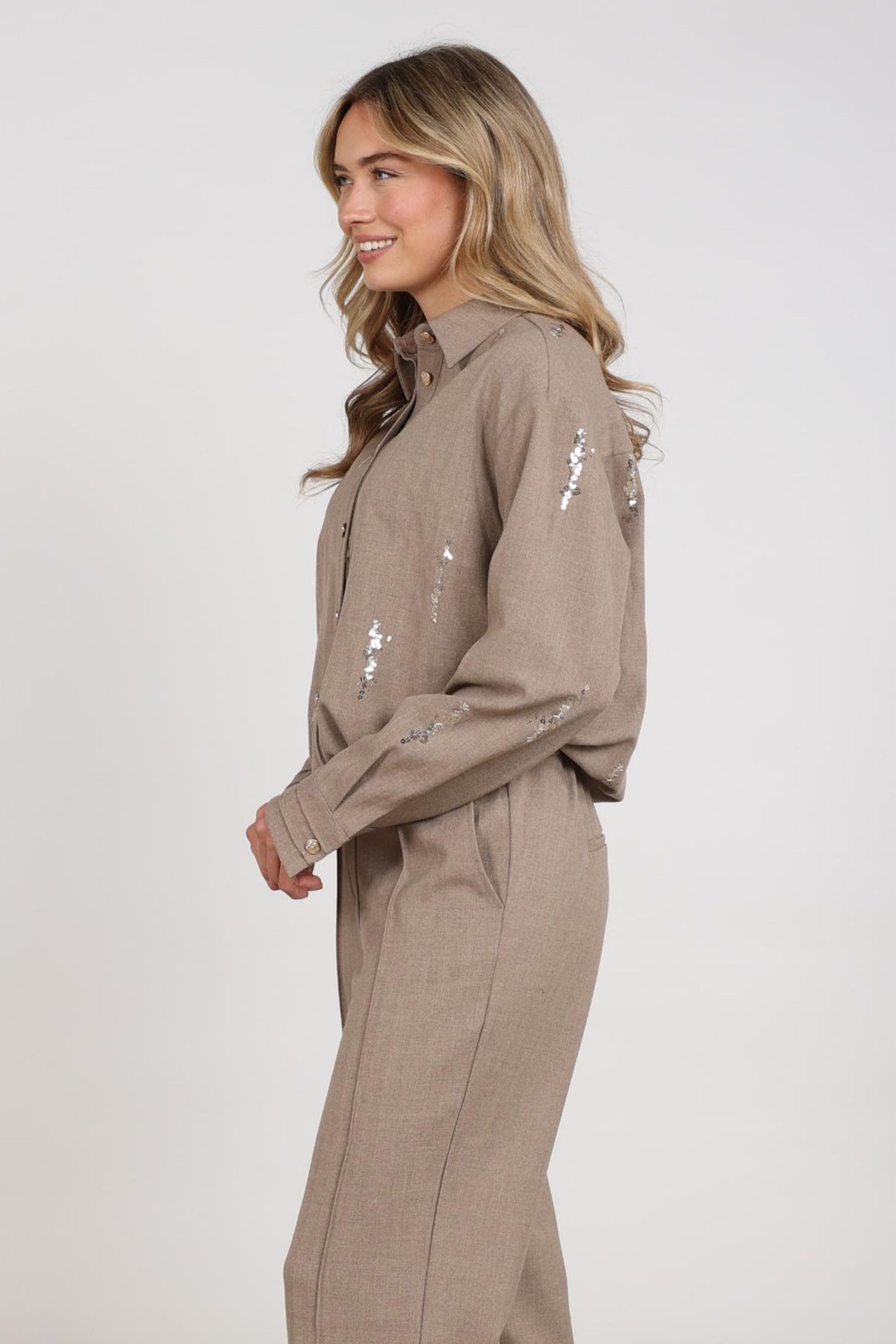 Taupe Nukus Annelynn pailletten blouse met lange mouwen en elegante details, gedragen door een model.