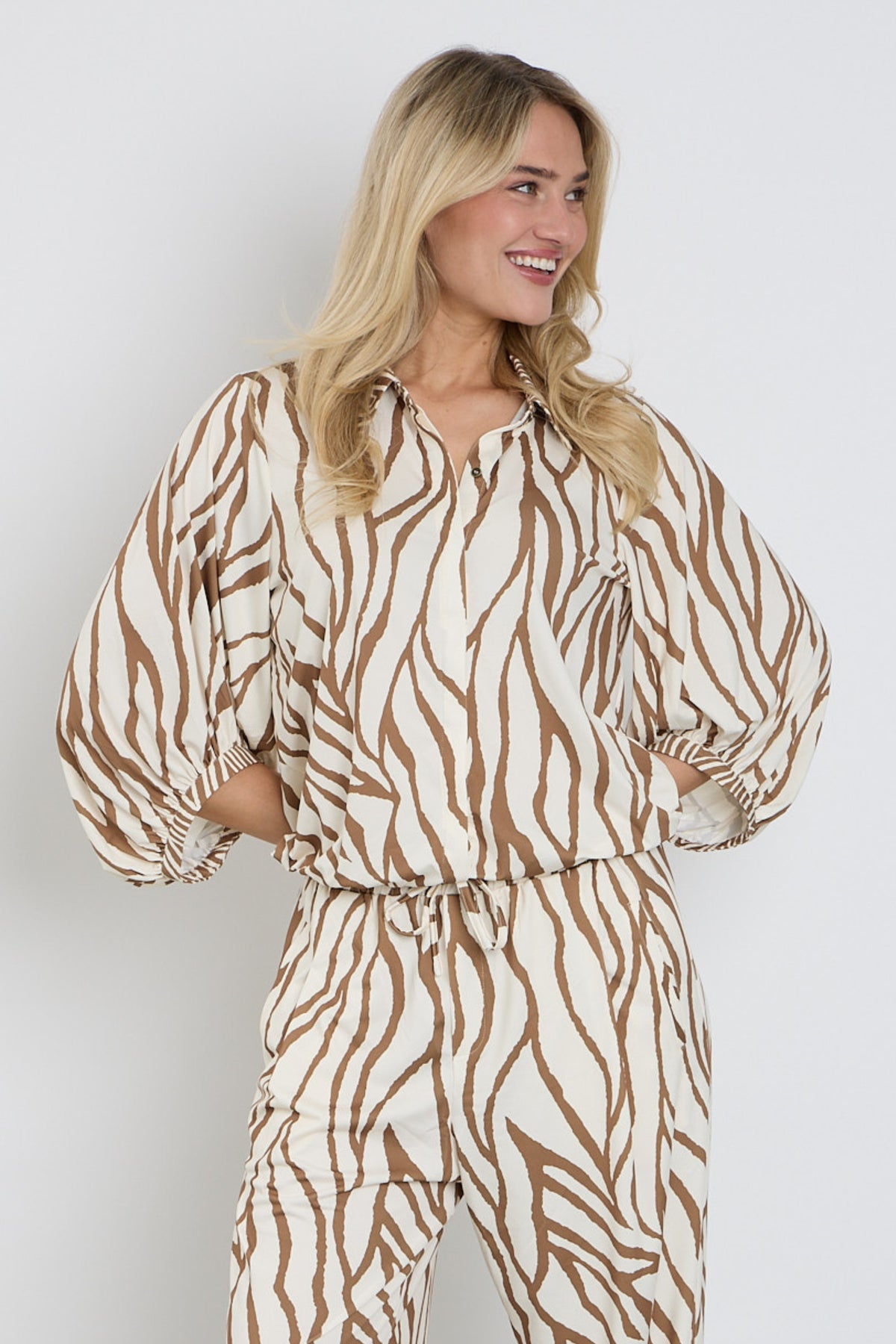 Blouse met design van K-design, met kleurrijke patronen en details, gedragen door model op witte achtergrond.