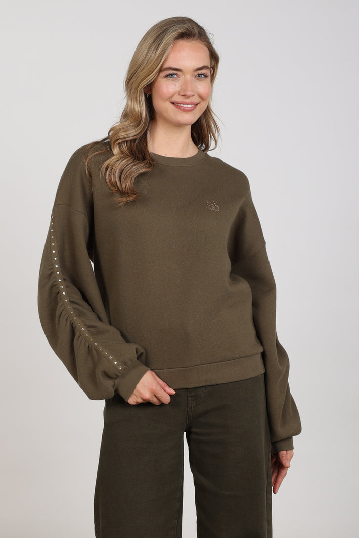 Nukus Trui Olivia Studs Moss met zachte stof en stijlvolle pasvorm, gedragen door een model tegen een neutrale achtergrond.