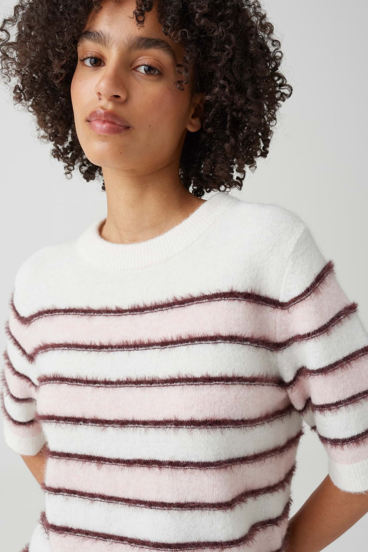 Roze getinte top van Opus met strepen, model Pimota Stripe, gedragen door een persoon in een stijlvolle setting.