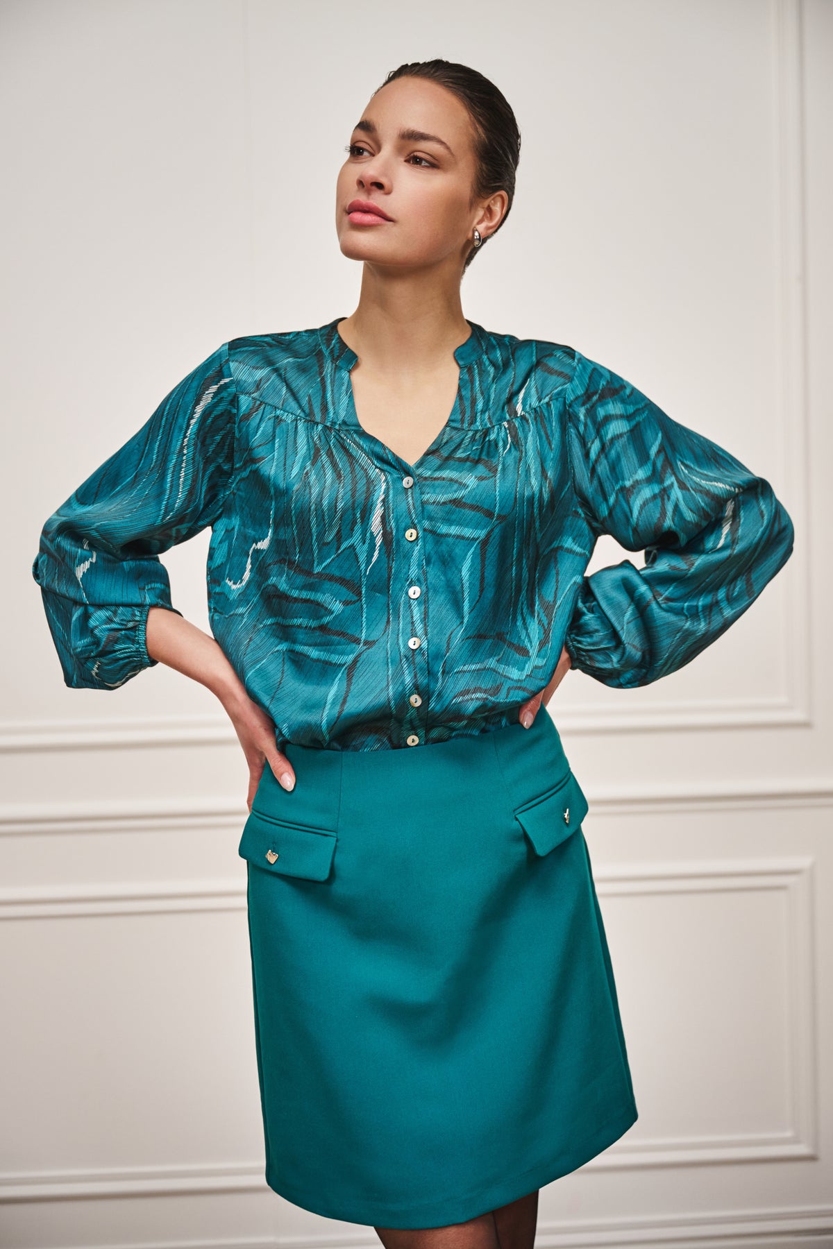 Kort teal rok van EsQualo met stadsprint en tailleband, gedragen door model met witte top.