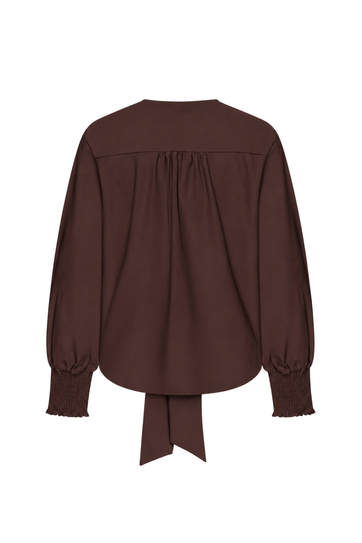 Mi Piace Travel Top Knotted Espresso, stijlvolle top met knoopdetail, gedragen door een model op een neutrale achtergrond.