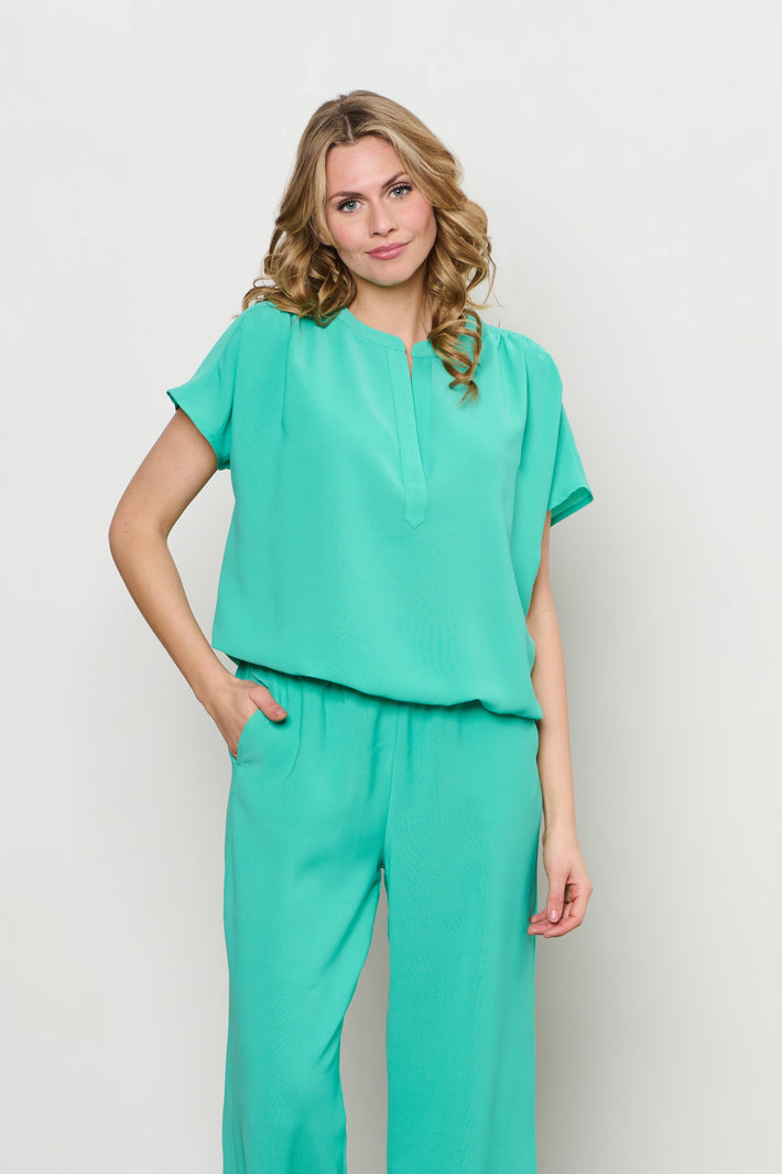 Blouse van &Co woman, Top Nola in aqua groen, met korte mouwen en ronde hals, gedragen door een model.
