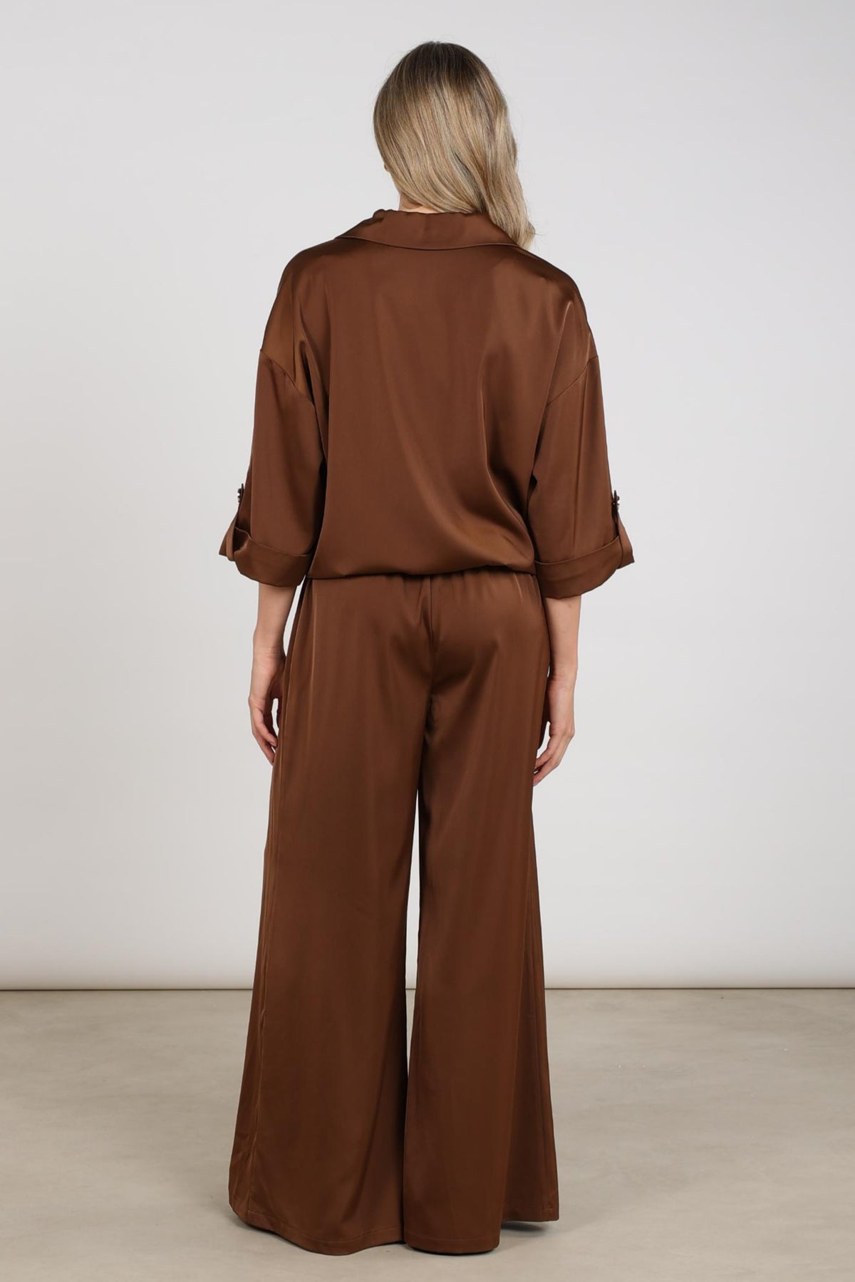Nukus broek June Shiny Espresso, glanzende zwarte damesbroek met elegante pasvorm, zichtbaar voor damesmode.