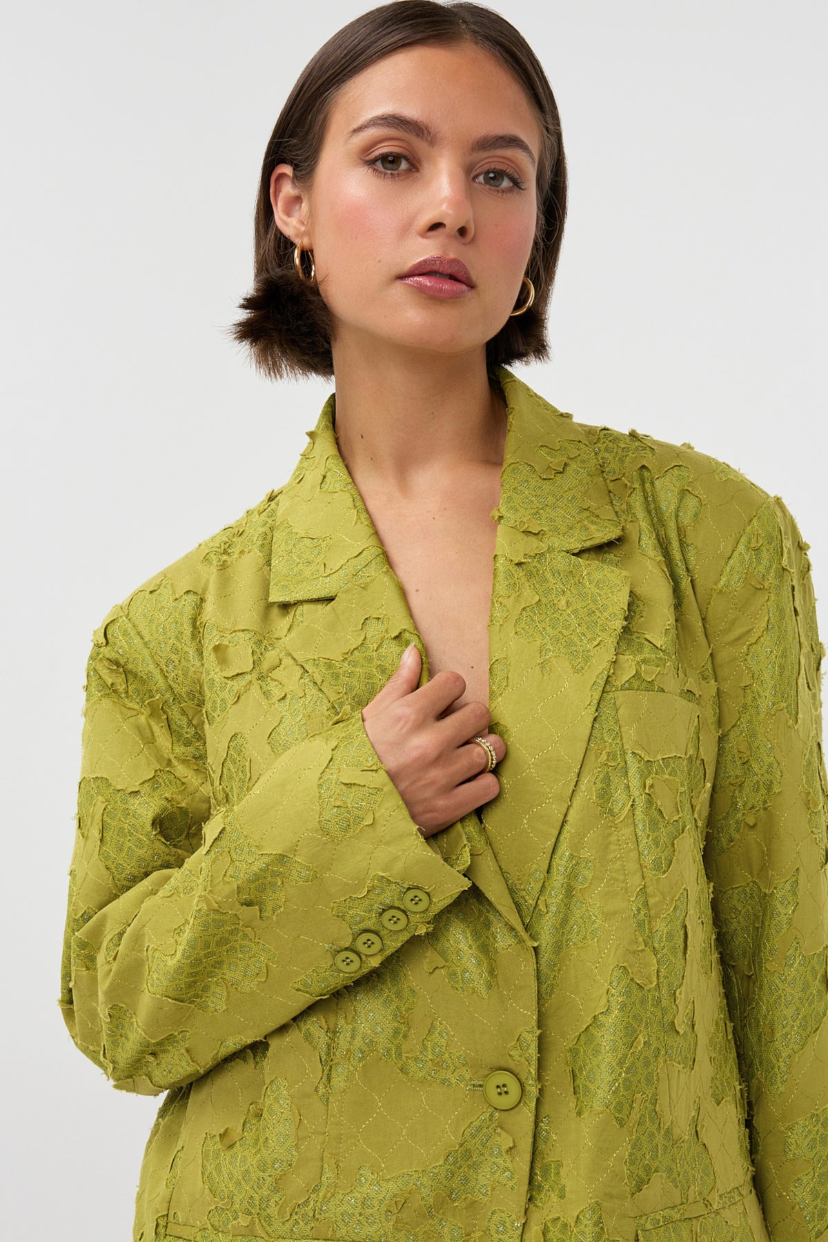 Groene blazer van Studio Amaya, model Mio, hangend aan een kledinghanger met een neutrale achtergrond.